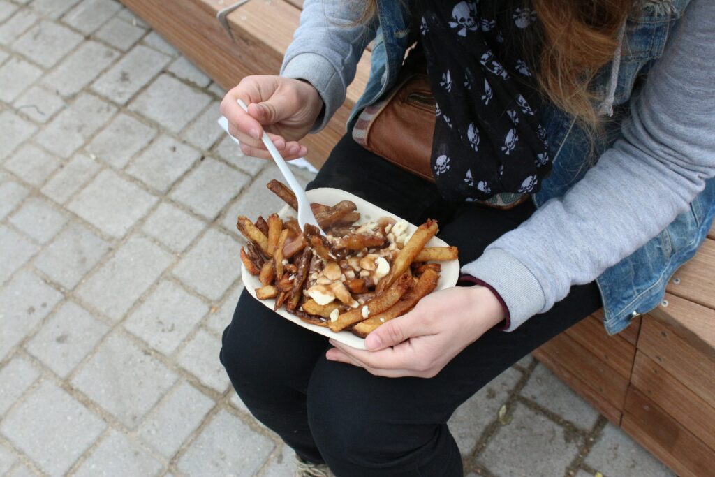 A person sitting on a bench with a paper tray of french fries covered in gravy and cheese curds.