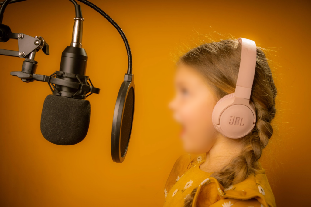A child with wireless headphones on speaking into a professional-looking microphone. The child's face has intentional blurring for privacy.