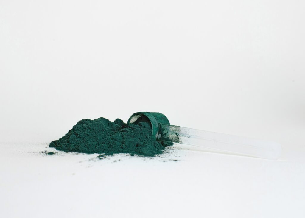 A scoop of a green-coloured supplement powder that was spilled out onto a white surface.